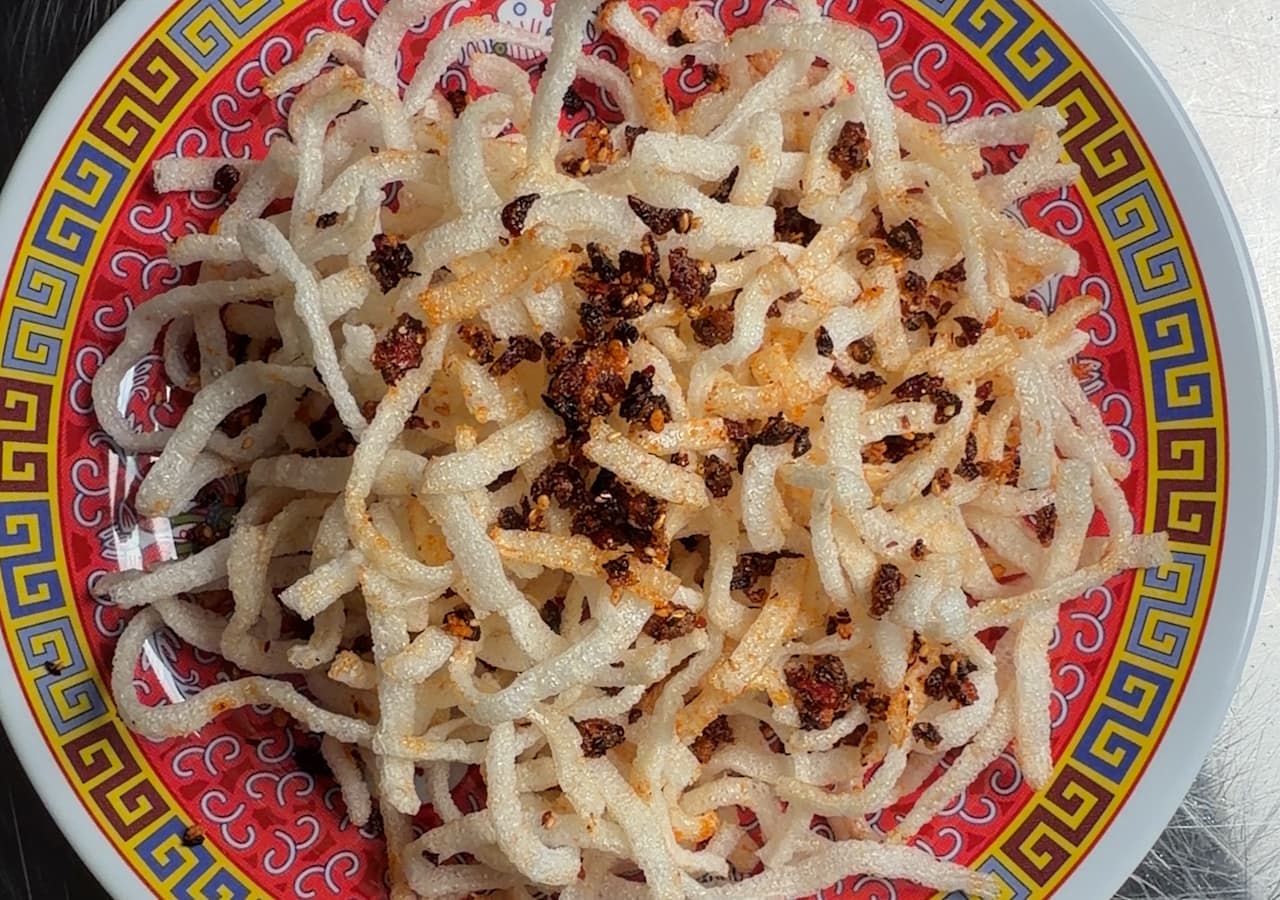Spicy Rice Noodle Crackers: Dry pad thai rice noodles dropped into hot oil where they instantly puff into airy, crunchy clouds. Seasoned with a savory-spicy chili crisp blend and served with a soy-lime dipping sauce.